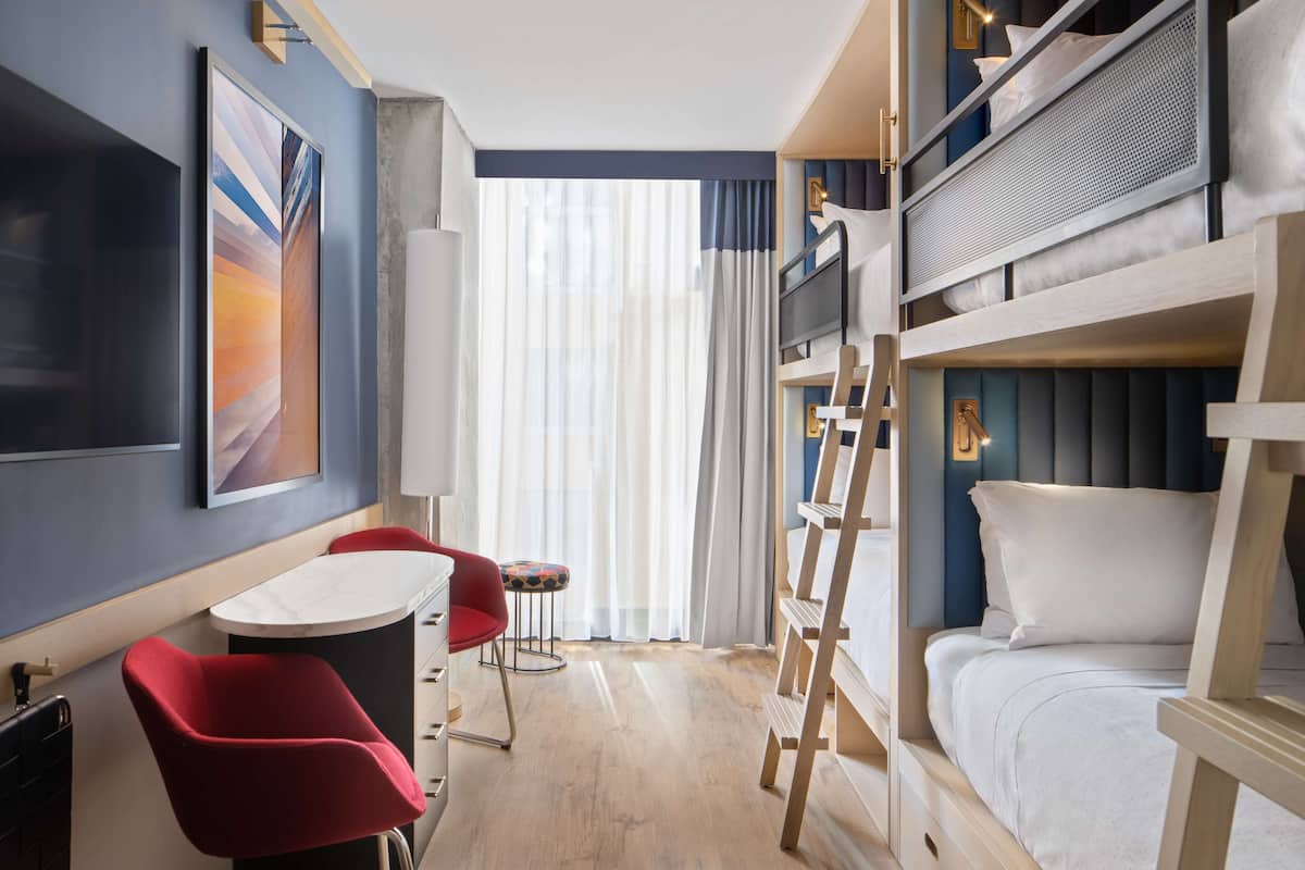 Ein Hotelzimmer mit einem Etagenbett, einem Schreibtisch mit Stuhl, einem kleinen Tisch und einem roten Sessel.