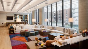 A spacious hotel lobby with a modern design, featuring a large seating area, a bar, and large windows offering city views. - Motto by Hilton New York City Chelsea (New York)