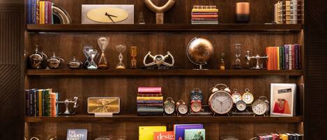 Una estantería de madera con varios libros, relojes y objetos decorativos.