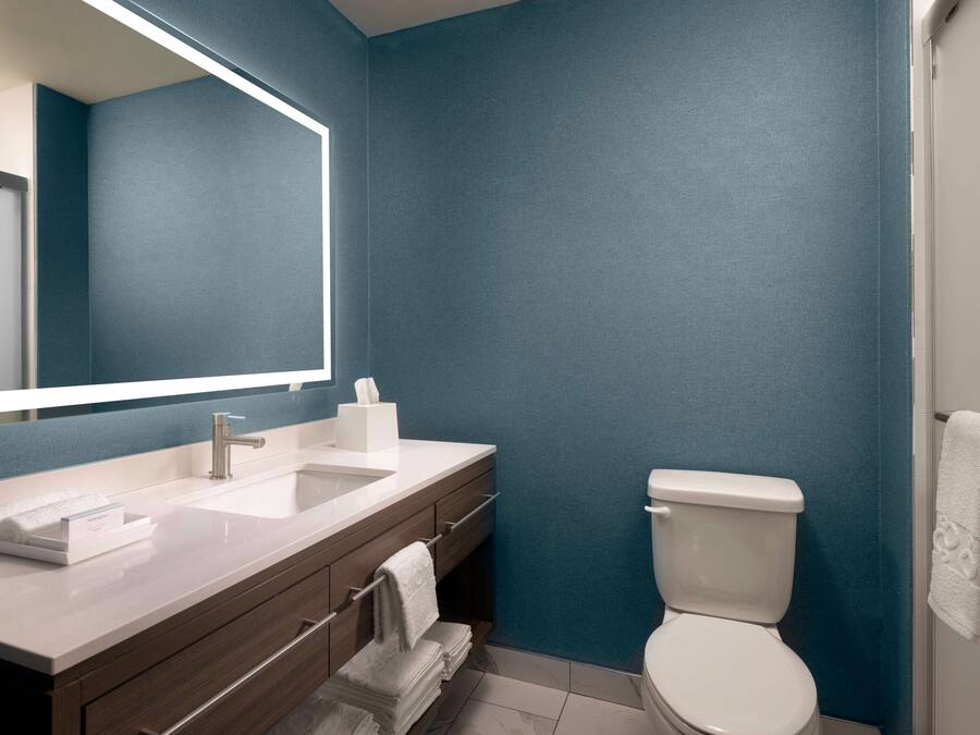 A modern bathroom with a large mirror, two sinks, a toilet, and a towel rack.