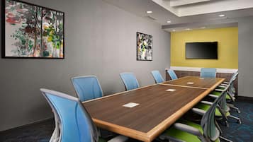 Uma sala de conferências com uma mesa comprida, cadeiras azuis e verdes, e duas pinturas abstratas nas paredes.