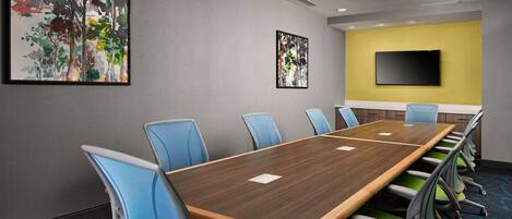 A conference room with a long table, blue and green chairs, and two abstract paintings on the walls.