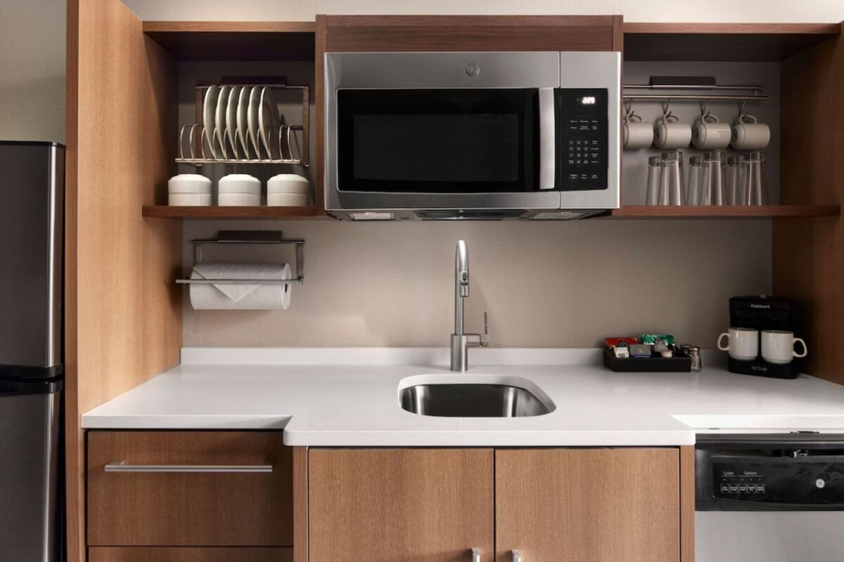 A modern kitchen with a stainless steel microwave, a sink, and wooden cabinets.