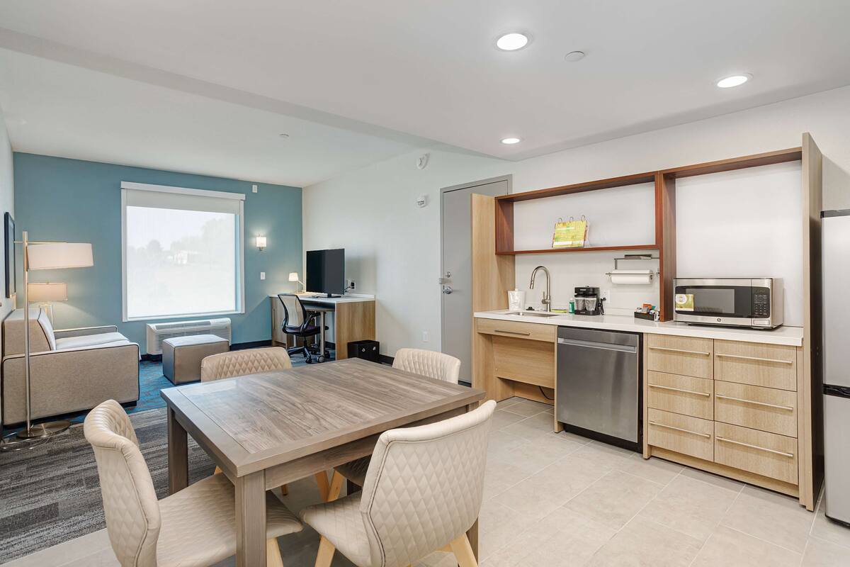 Une chambre d’hôtel moderne dotée d’un coin repas, d’une kitchenette et d’une grande fenêtre.