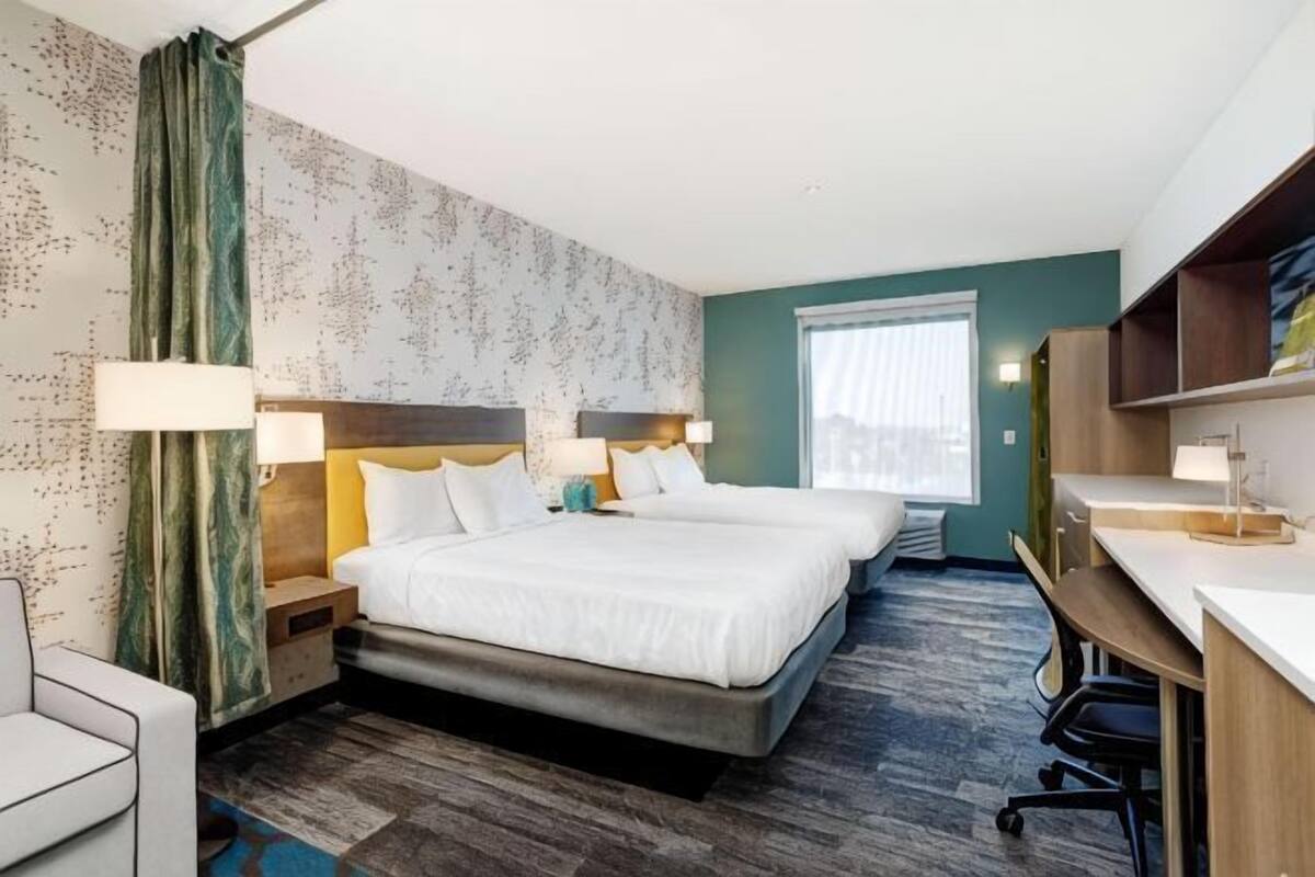 Une chambre d’hôtel avec deux lits, un bureau, une chaise et une fenêtre.