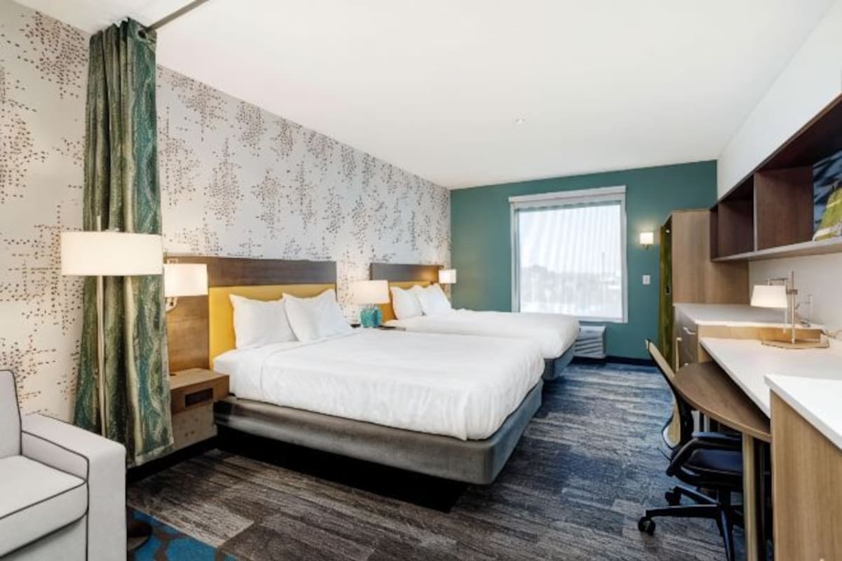 Een hotelkamer met twee bedden, een bureau, een stoel en een raam.
