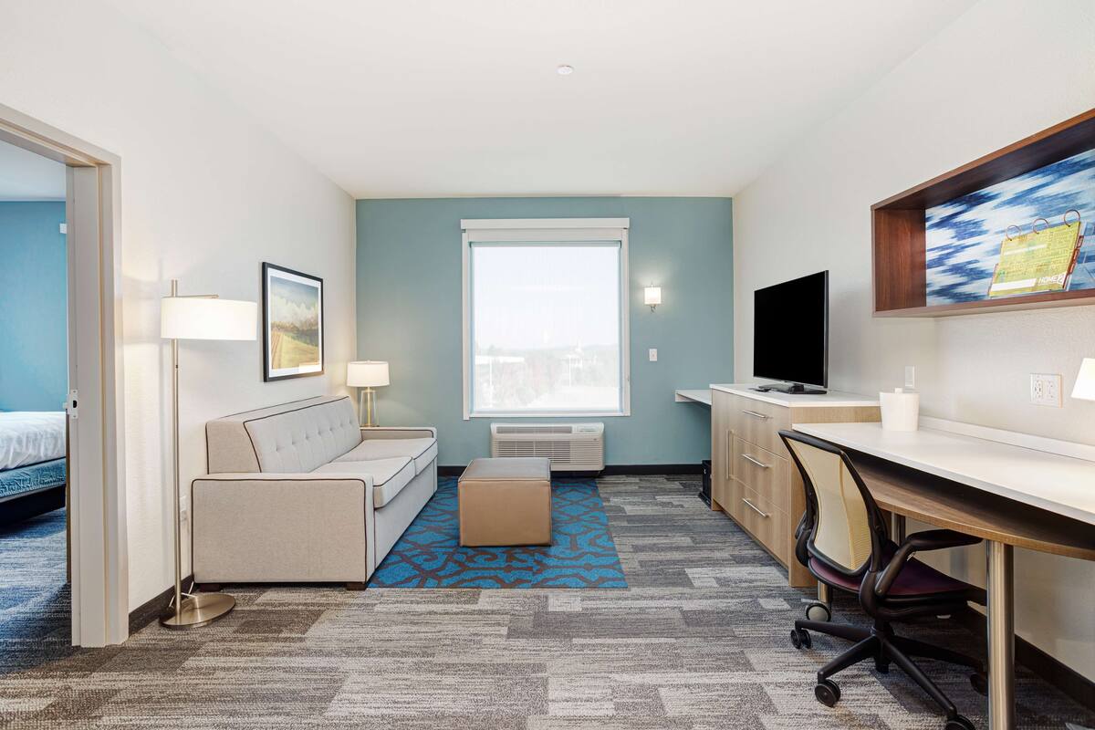Une chambre d’hôtel équipée d’un lit, d’un canapé, d’un bureau, d’une chaise, d’une télévision et d’une grande fenêtre.