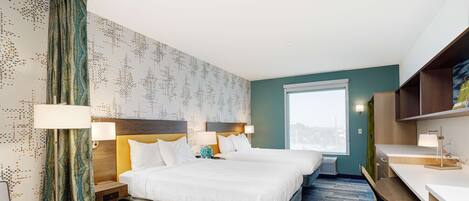 A hotel room with two beds, a desk, and a view of the city.
