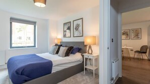Een moderne slaapkamer met een groot bed, nachtlampjes en kunst aan de muur.
