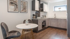 Een moderne keuken met grijze kasten, een wit aanrecht en een ronde tafel met stoelen. Er hangen twee kunstwerken aan de muur.