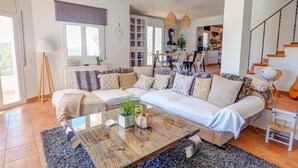 Uma sala de estar moderna com um amplo sofá em forma de L, uma mesa de centro de vidro e uma área de jantar com mesa e cadeiras de madeira.