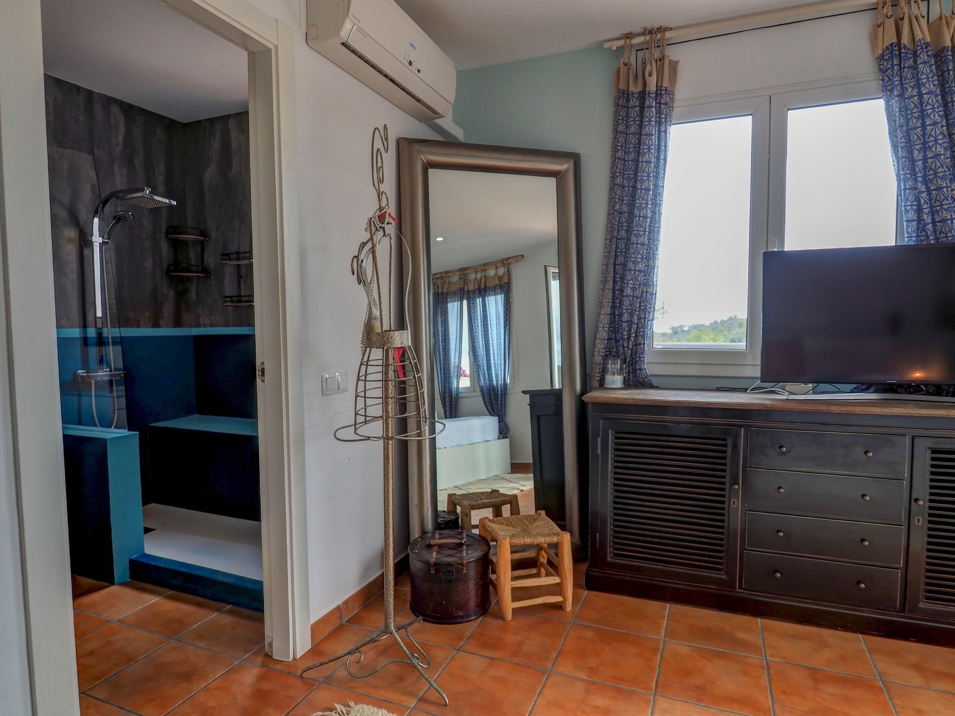 Un espacio habitable compacto con kitchenette, televisor y un taburete pequeño.