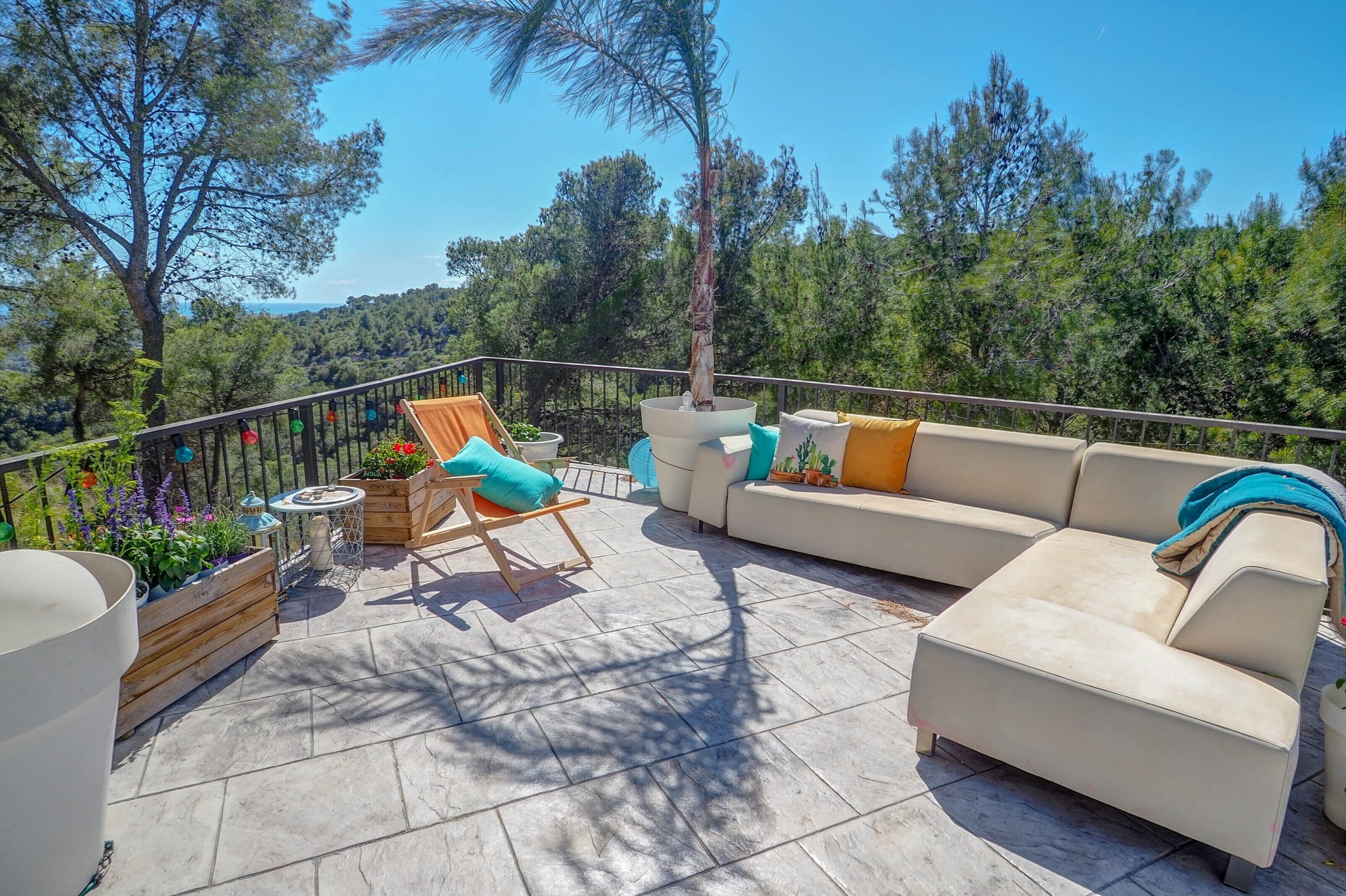 A sunlit outdoor seating area with a beige sofa, a wooden chair, and a small table.