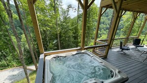 A hot tub on a wooden deck with a view of a forest.