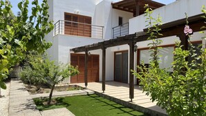 Une maison moderne à deux étages, dotée d’un patio couvert, d’une petite pelouse et de diverses plantes.