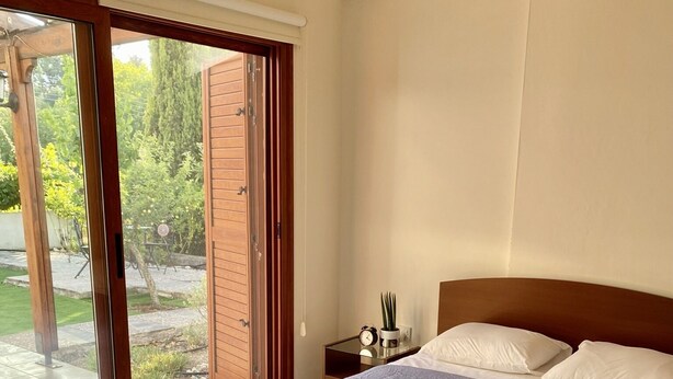 Une chambre avec deux lits, une porte-fenêtre coulissante donnant sur une terrasse, et une table de chevet avec une horloge et une plante.