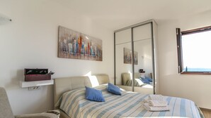 Een slaapkamer met een bed, een stoel, een nachtkastje, een spiegel en een schilderij aan de muur.