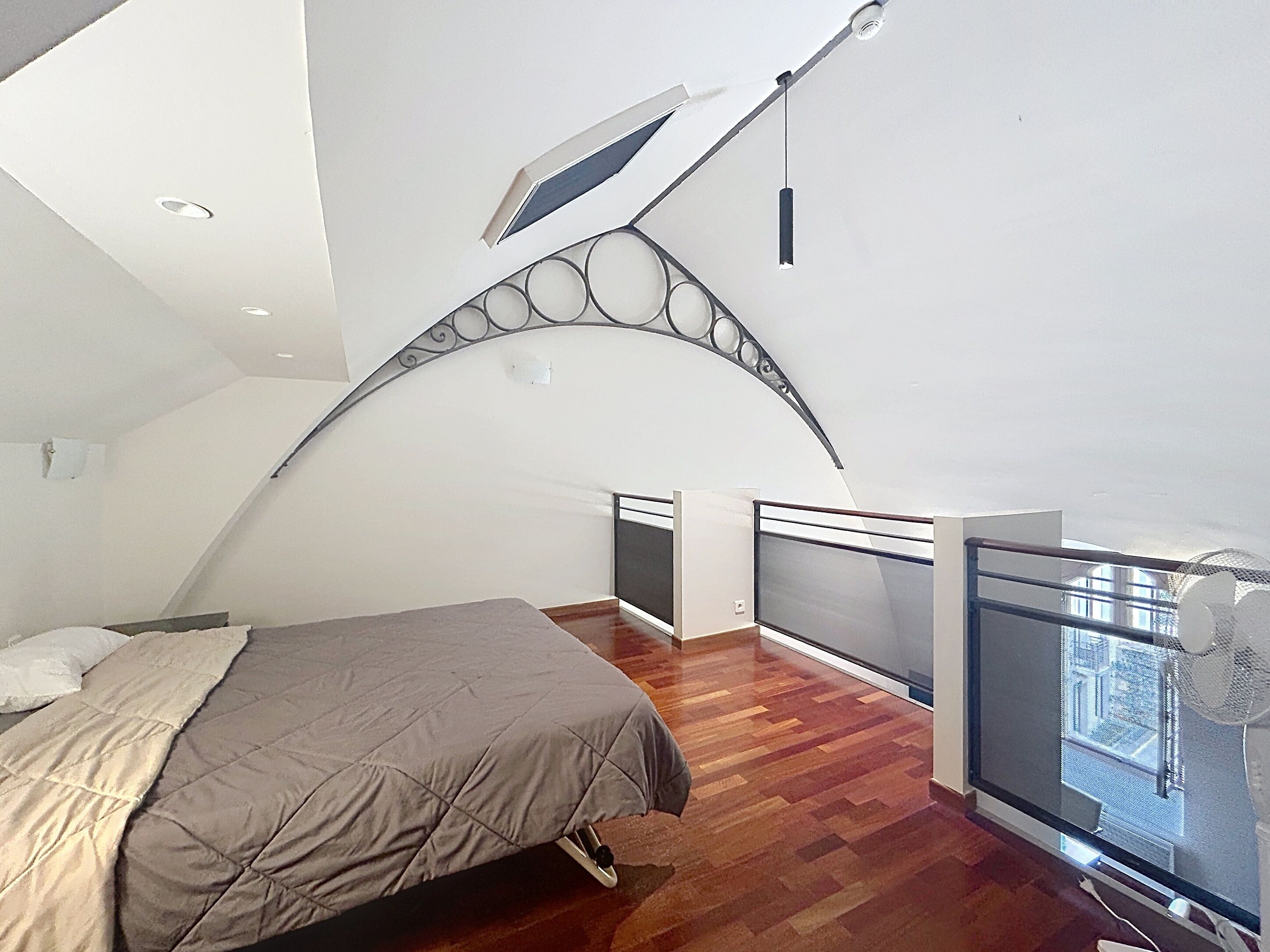 A bedroom with a bed, a window, and a balcony with a railing.