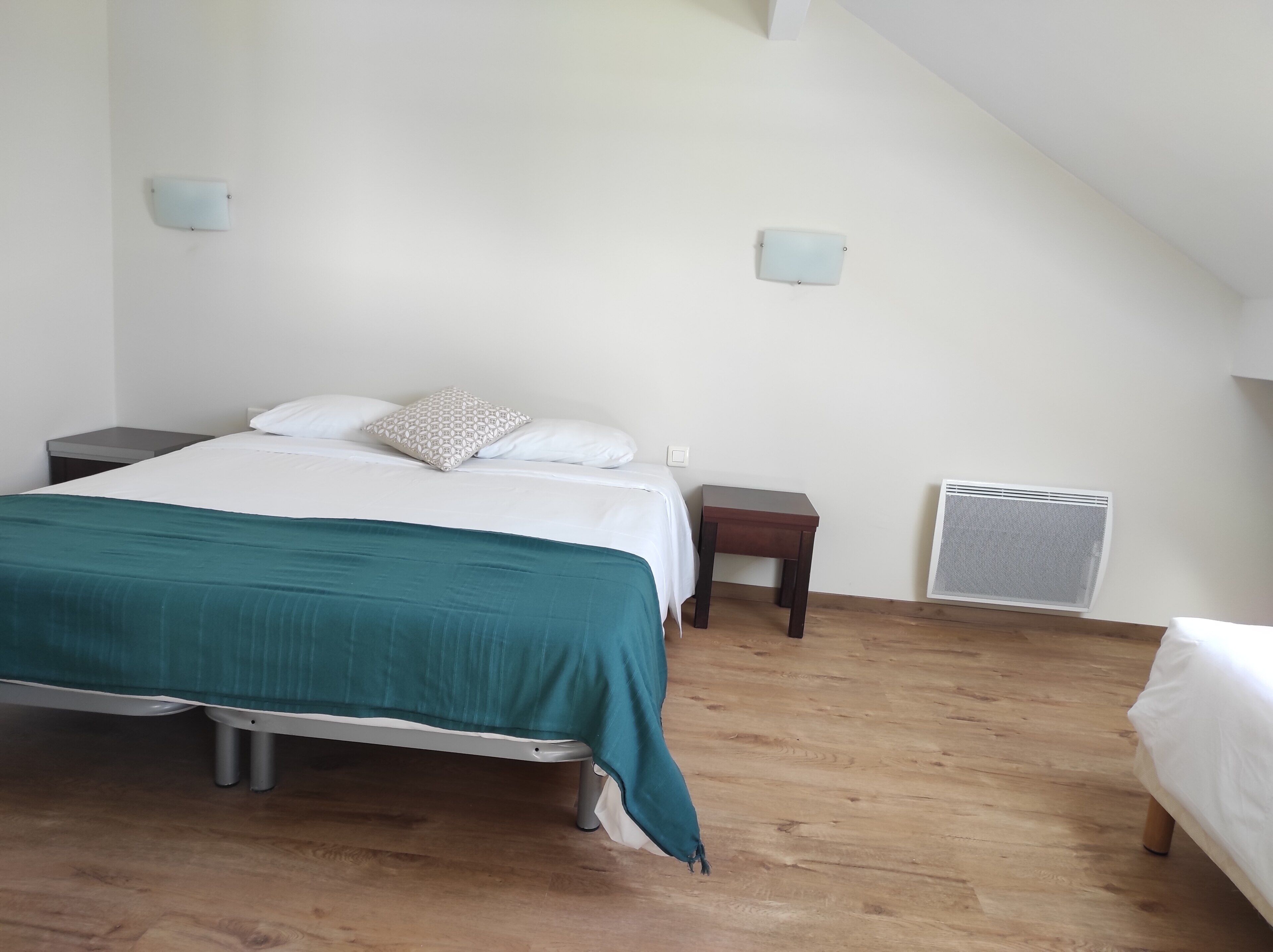 A bedroom with a bed, bedside tables, a heater, and a sloped ceiling.