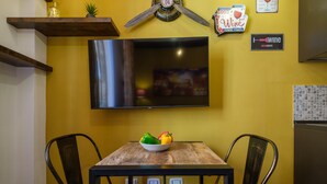 A dining area with a wooden table, two chairs, a bowl of fruit, a flat-screen TV mounted on the wall, and a refrigerator. - Casa del sole by Studio Vita (Bologna)
