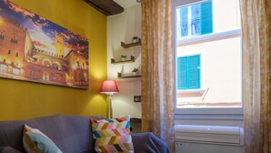 A room with a sofa, colorful pillows, a lamp, a painting of a historical building, and a window with curtains. - Casa del sole by Studio Vita (Bologna)