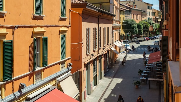 A narrow street with outdoor seating and tables, surrounded by buildings with balconies and shutters. - Casa del sole by Studio Vita (Bologna)