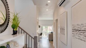Ein Flur mit Treppe, einem Blumentopf, einem Spiegel und gerahmten Kunstwerken an den Wänden.