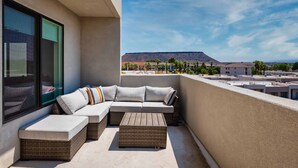 Ein Balkon mit Ecksofa, einem kleinen Tisch und einem großen Fenster.