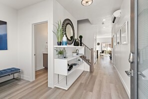 Stylish hallway with a console table, shelving units, and a bench, leading to a staircase with a glass railing.