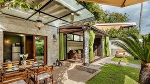 Un patio con mesa y sillas de madera, cerramiento de vidrio y vista al interior de la casa.