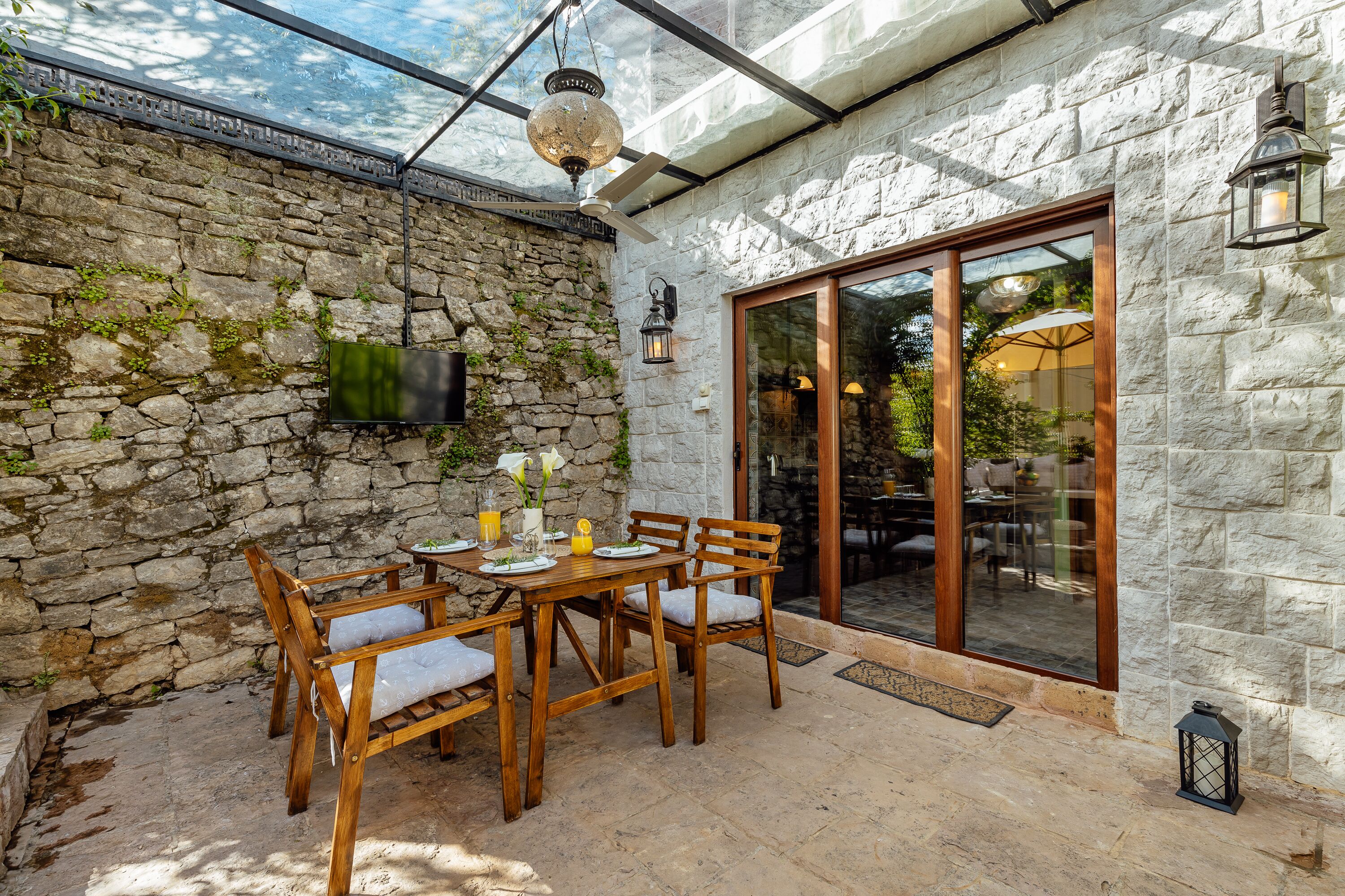 Un mur en pierre, une table et des chaises en bois, un téléviseur fixé au mur et une porte vitrée donnant sur un espace extérieur.