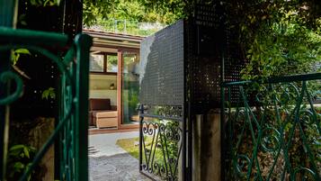 A gated entrance to a residential property with a metal gate, a pathway leading to a glass door, and a small garden area with greenery.