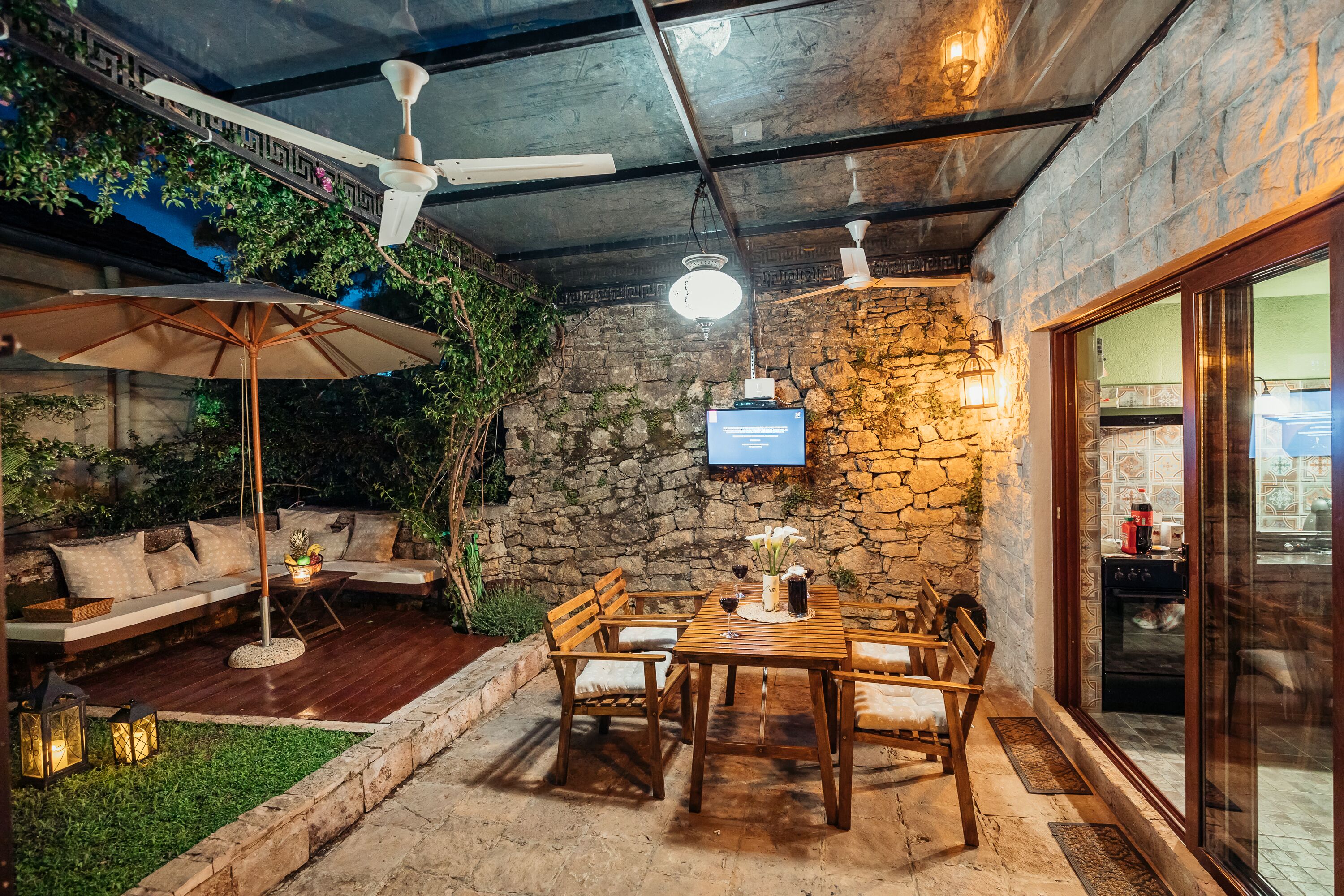 A cozy outdoor seating area with wooden furniture, a stone wall, and a television mounted on the wall.