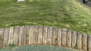 A playground with a slide and climbing structures, surrounded by a wooden fence and a paved path. - The Crail Maltings (Anstruther)
