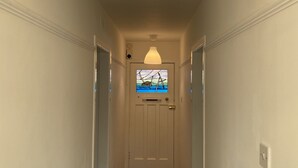 A hallway with a white door at the end, a large white pendant light above, and a small window with a view of the sky and clouds. - The Crail Maltings (Anstruther)