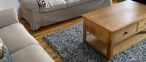 Un salon avec un canapé beige, une table basse en bois et un tapis à motifs.