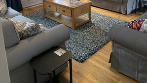 A modern living room with a grey sofa, a wooden coffee table, and a black and white rug. There is a painting on the wall and a window with curtains. - The Crail Maltings (Anstruther)