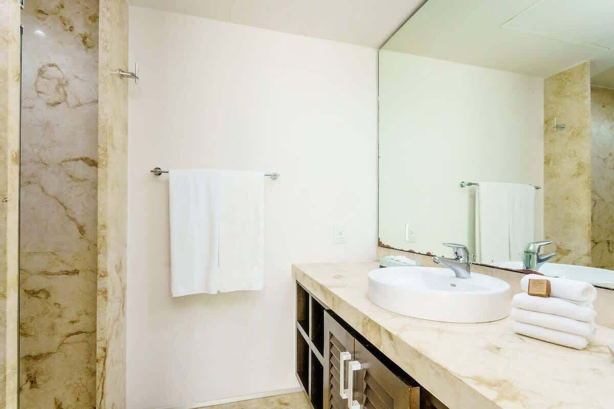 A modern bathroom with a marble wall, a round sink, a large mirror, and a towel rack.