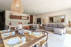 A modern living room with a dining area, a sofa, and a kitchen in the background.