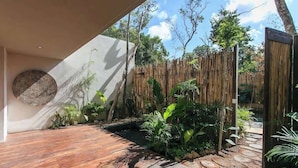 A modern outdoor space with a wooden deck, a bamboo fence, and various tropical plants. - Aldea Zama Condo: Private Pool and Jungle Views (Tulum)