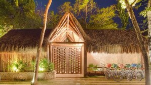 A thatched-roof building with a wooden door, surrounded by trees and a bicycle parked outside. - Aldea Zama Condo: Private Pool and Jungle Views (Tulum)