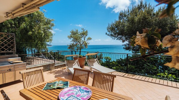 A terrace with a view of the sea, outdoor furniture, and a grill.