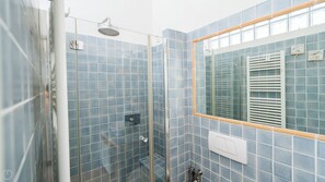 A shower with a glass door, a mirror, and a tiled wall.