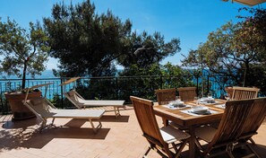 An outdoor patio with a table set for dining, lounge chairs, and a view of the sea.