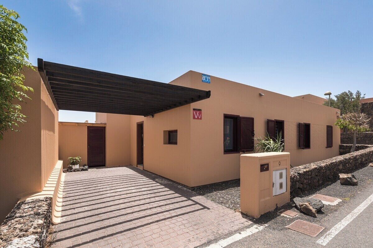A building with a covered entrance, a small garden area, and a paved driveway.