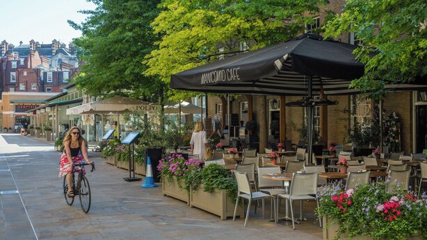 An outdoor cafe with tables and chairs, a cyclist, and potted plants. - First Street III by Onefinestay (London)