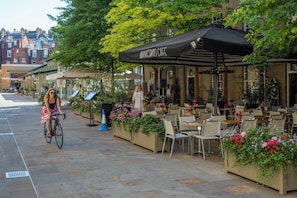 An outdoor cafe with tables and chairs, a cyclist, and potted plants. - First Street III by Onefinestay (London)