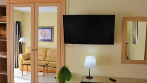 Une chambre d’hôtel équipée d’un téléviseur fixé au mur, d’une lampe de chevet, d’un canapé et d’un grand miroir.