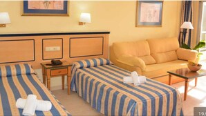 Une chambre d’hôtel avec deux lits, un canapé, une petite table et une lampe.