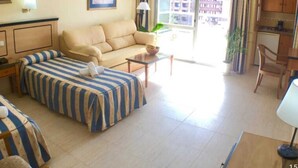 Une chambre d’hôtel avec un lit, un canapé, une petite table et une fenêtre donnant sur des immeubles.